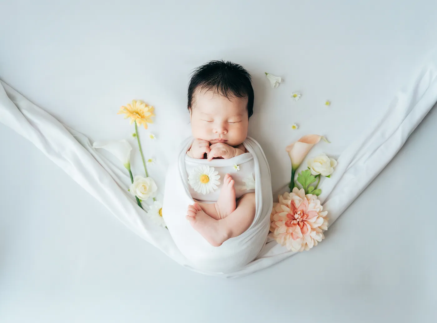 白い布に包まれ花に囲まれて眠る新生児